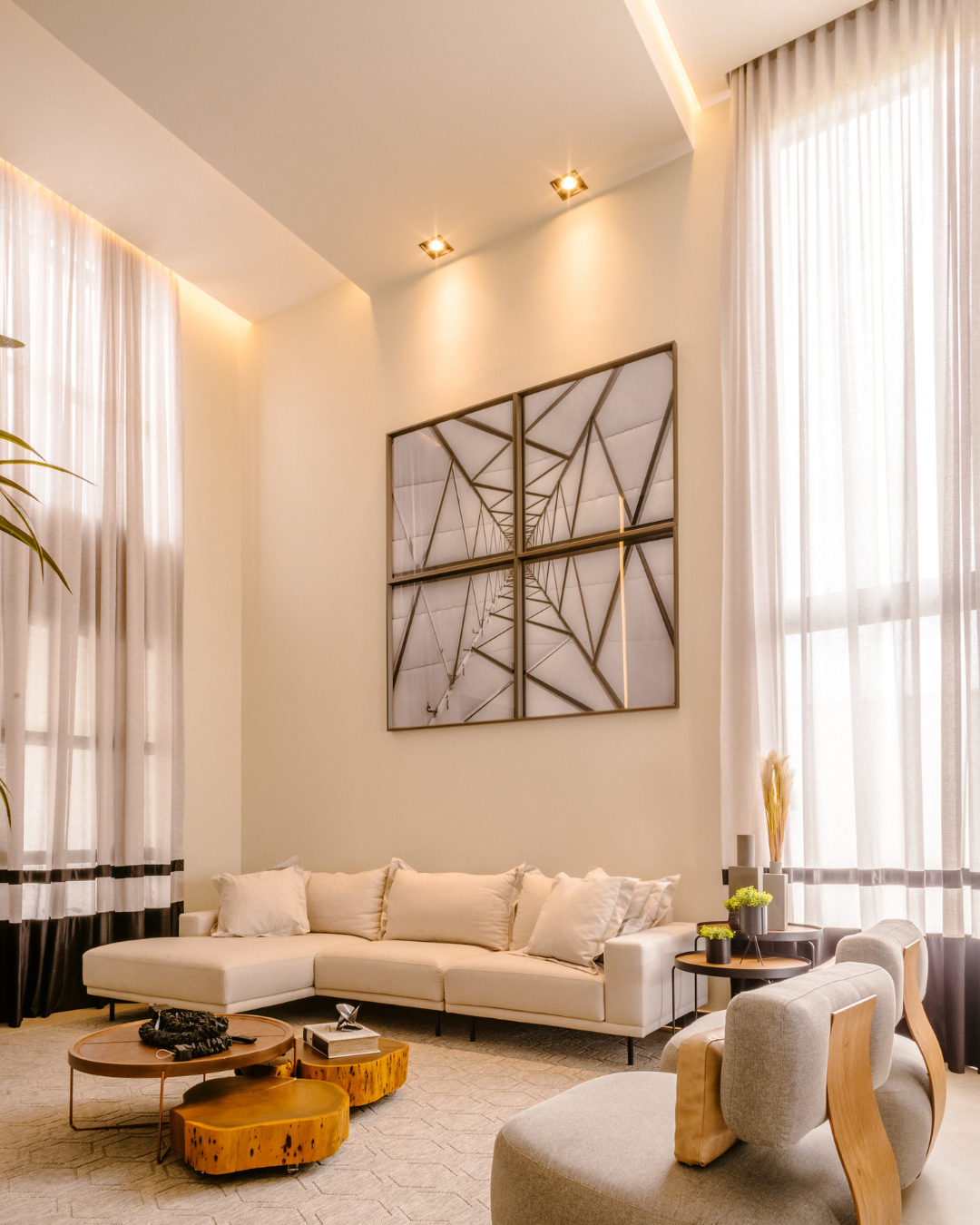 Modern minimalist living room featuring a white sectional sofa, light wood accent tables, neutral armchairs, and floor-to-ceiling sheer curtains.